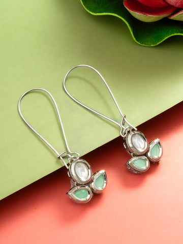 A pair of silver-toned drop earrings with oval and teardrop-shaped light green stones, displayed on a split green and coral background.