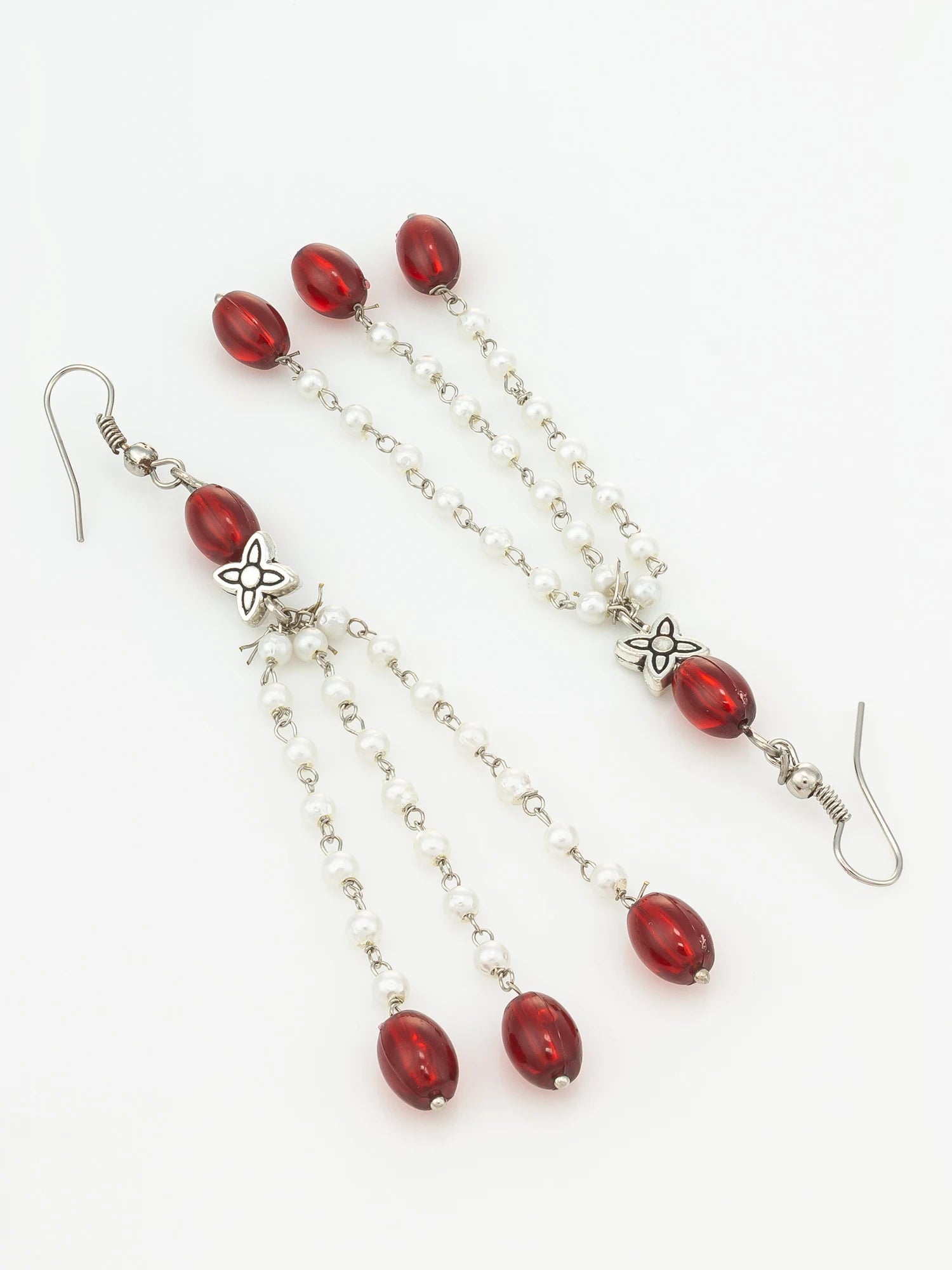 A pair of long dangle earrings with polished red oval beads, small white pearl-like beads on silver-tone chains, and silver-tone floral accents, shown on a plain white background.