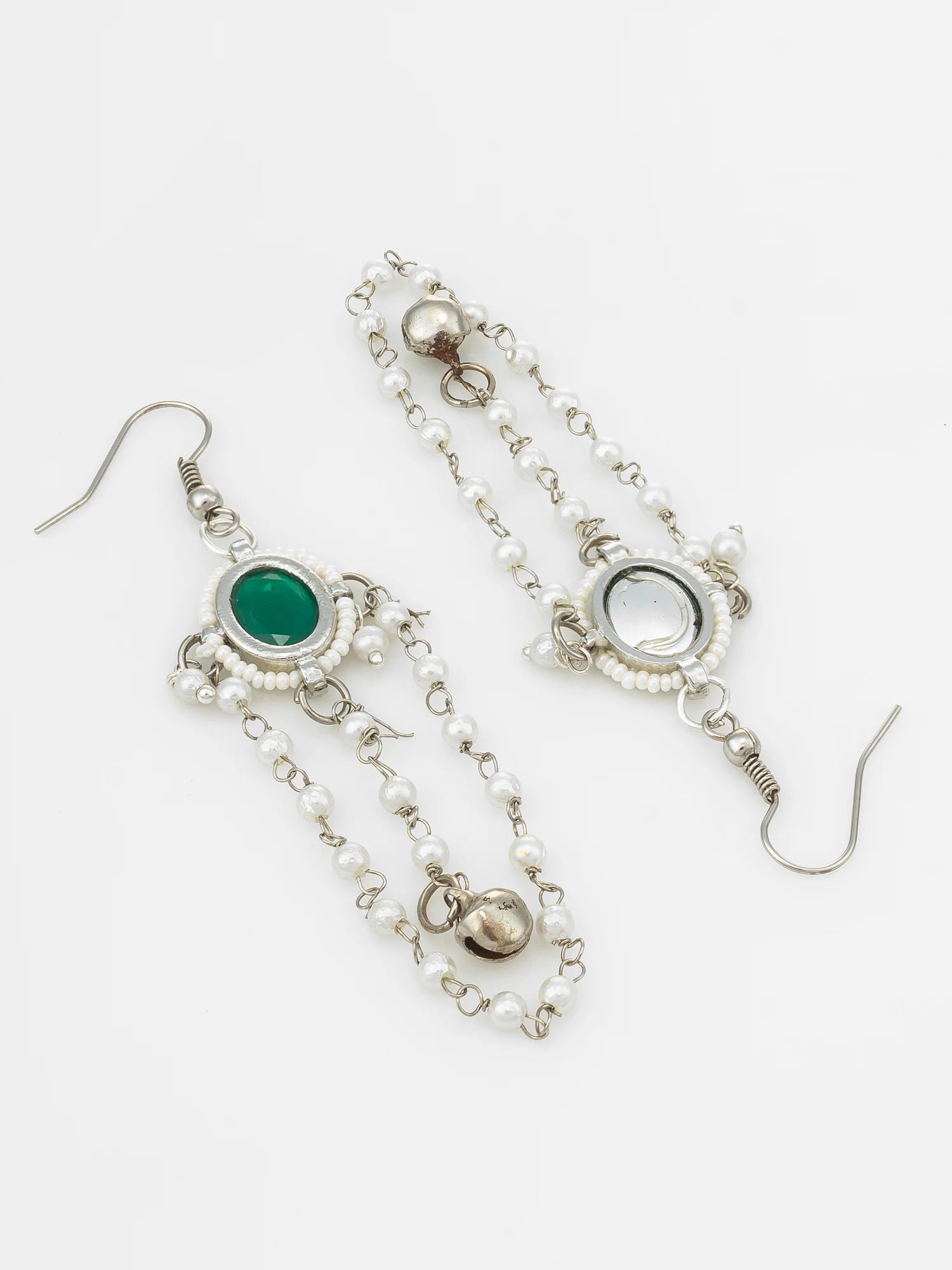 A pair of bohemian-style dangle earrings featuring silver-toned chains, small white faux pearls, and oval bezel-set stones, one green and one clear, on a plain white background.