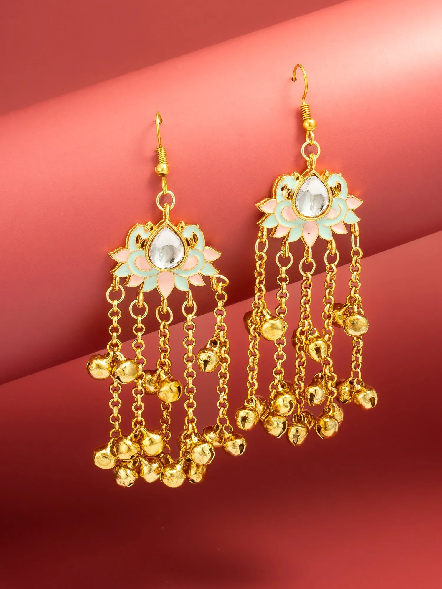 A pair of gold-toned dangle earrings with pastel mint green and pink enamel flower details, clear teardrop stones, and multiple dangling bell chains, displayed on a pink and red gradient background.