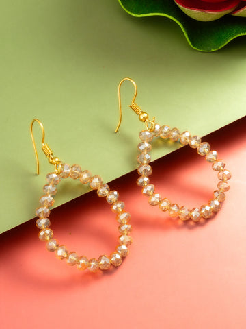 A pair of gold-tone drop earrings with faceted pearl-like beads, displayed on a split green and coral pink background.