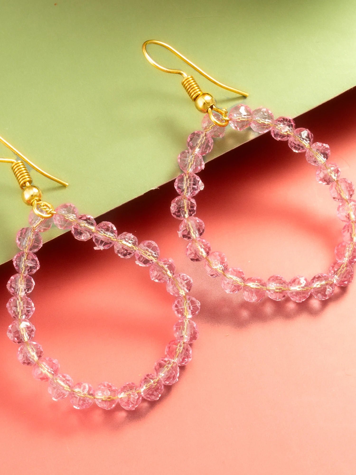 Pink beaded hoop earrings with gold fishhook ear wires, displayed on a split pastel green and coral pink background.