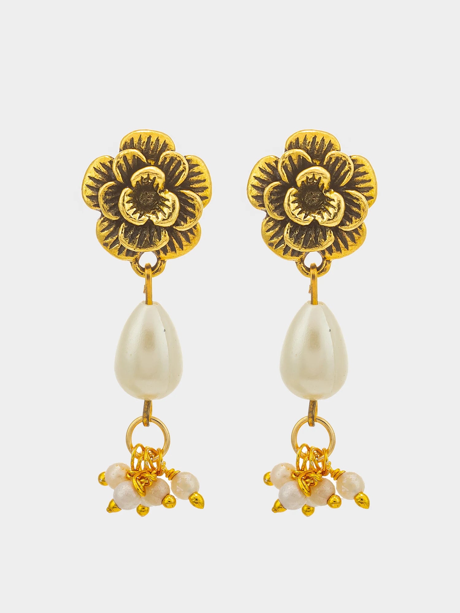 A pair of gold-toned dangle earrings featuring textured flower-shaped studs, teardrop-shaped white faux pearls, and small clustered pearl drops at the bottom, set against a light gray background.