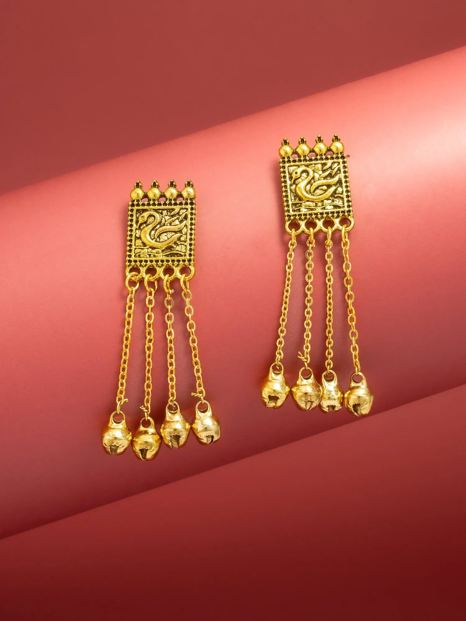 A pair of gold-toned Indian-style dangle earrings with intricate filigree work on a pink background.