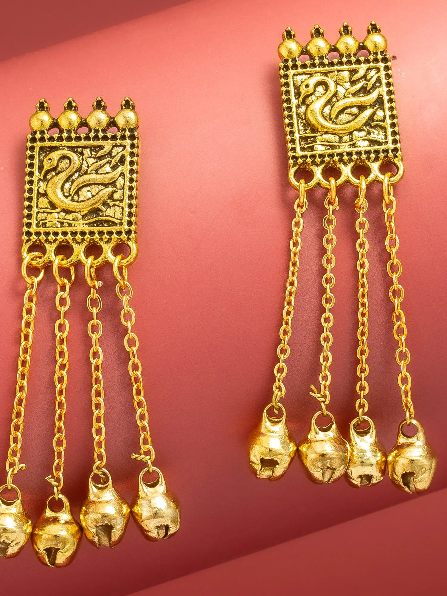 A pair of gold-toned Indian-style dangle earrings with intricate filigree work on a pink background.