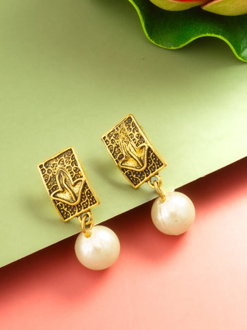 A pair of gold-toned drop earrings with rectangular filigree studs featuring a tulip motif and dangling white pearl beads, displayed on a split green and pink background with a leaf prop.