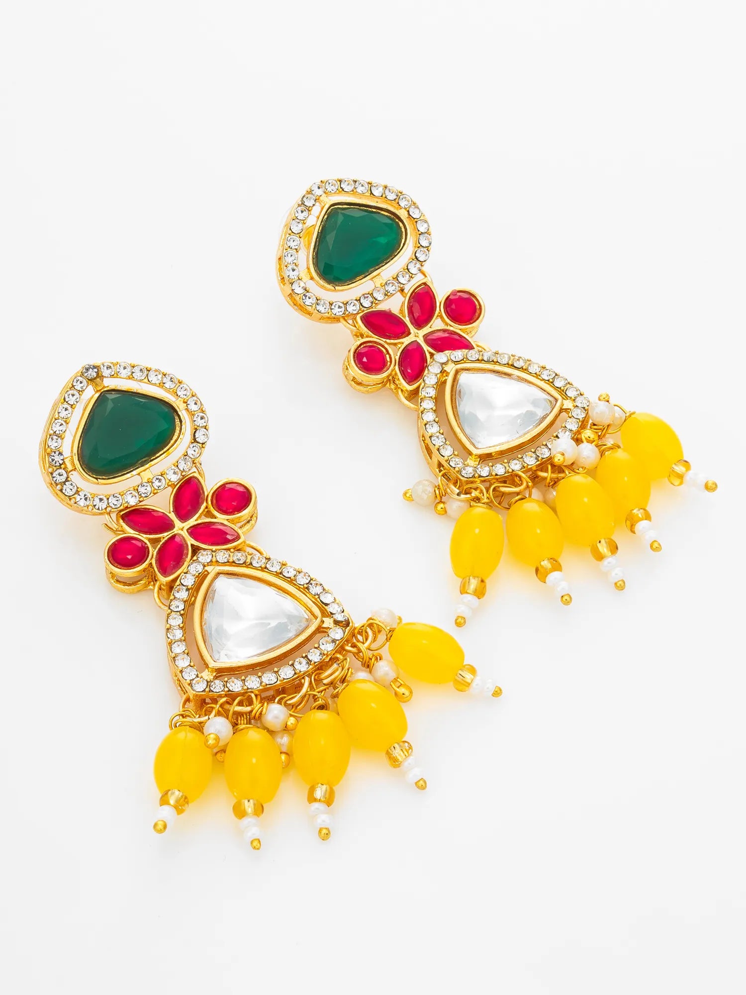 A pair of gold-plated Indian jhumka earrings featuring green heart-shaped stones, red flower motifs, white teardrop stones, and yellow bead drops, set against a plain white background.