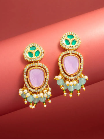 A pair of ornate gold-plated drop earrings with light purple oval stones, green enamel details, and dangling light green beads and white faux pearls, displayed on a curved red background.