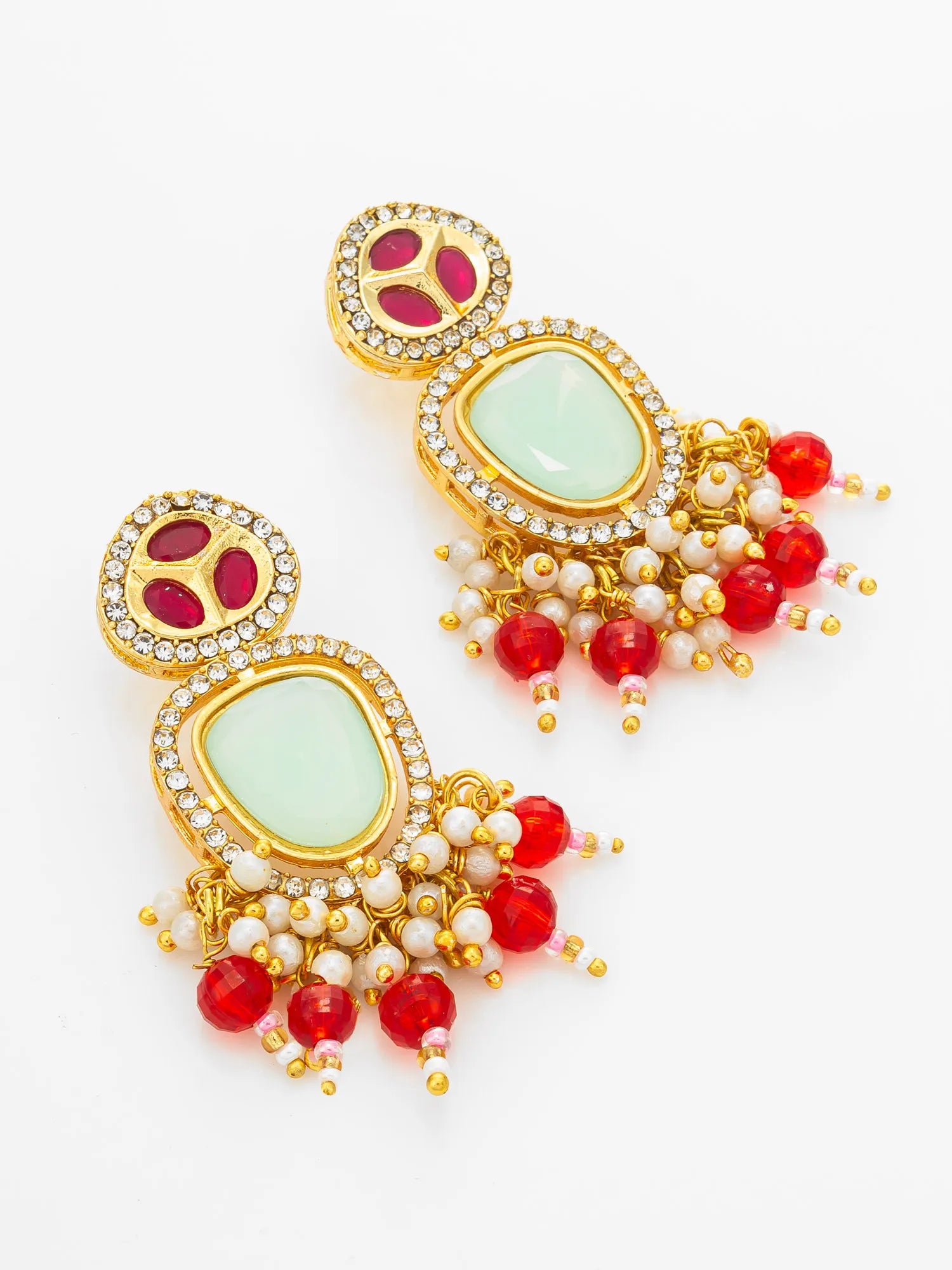 A pair of ornate gold-plated Indian-style earrings featuring light green stone centers, red bead drops, and white pearl-like beads, set against a plain white background.
