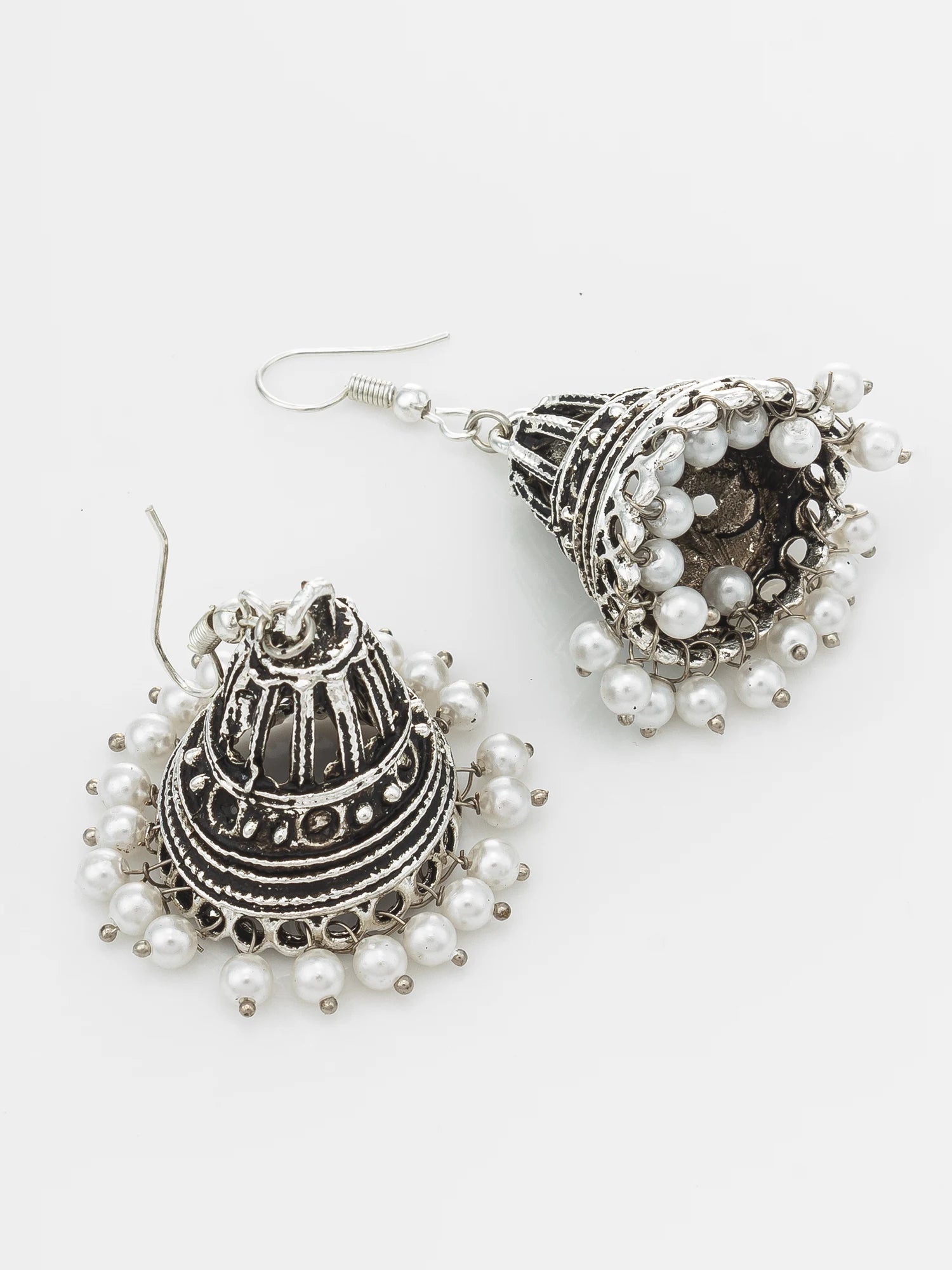 A pair of silver-toned jhumka earrings decorated with small white faux pearls, shown on a plain light gray background.