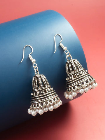 A pair of silver-toned bell-shaped dangle earrings with white pearl bead drops, displayed on a blue cylindrical prop against a pink background.