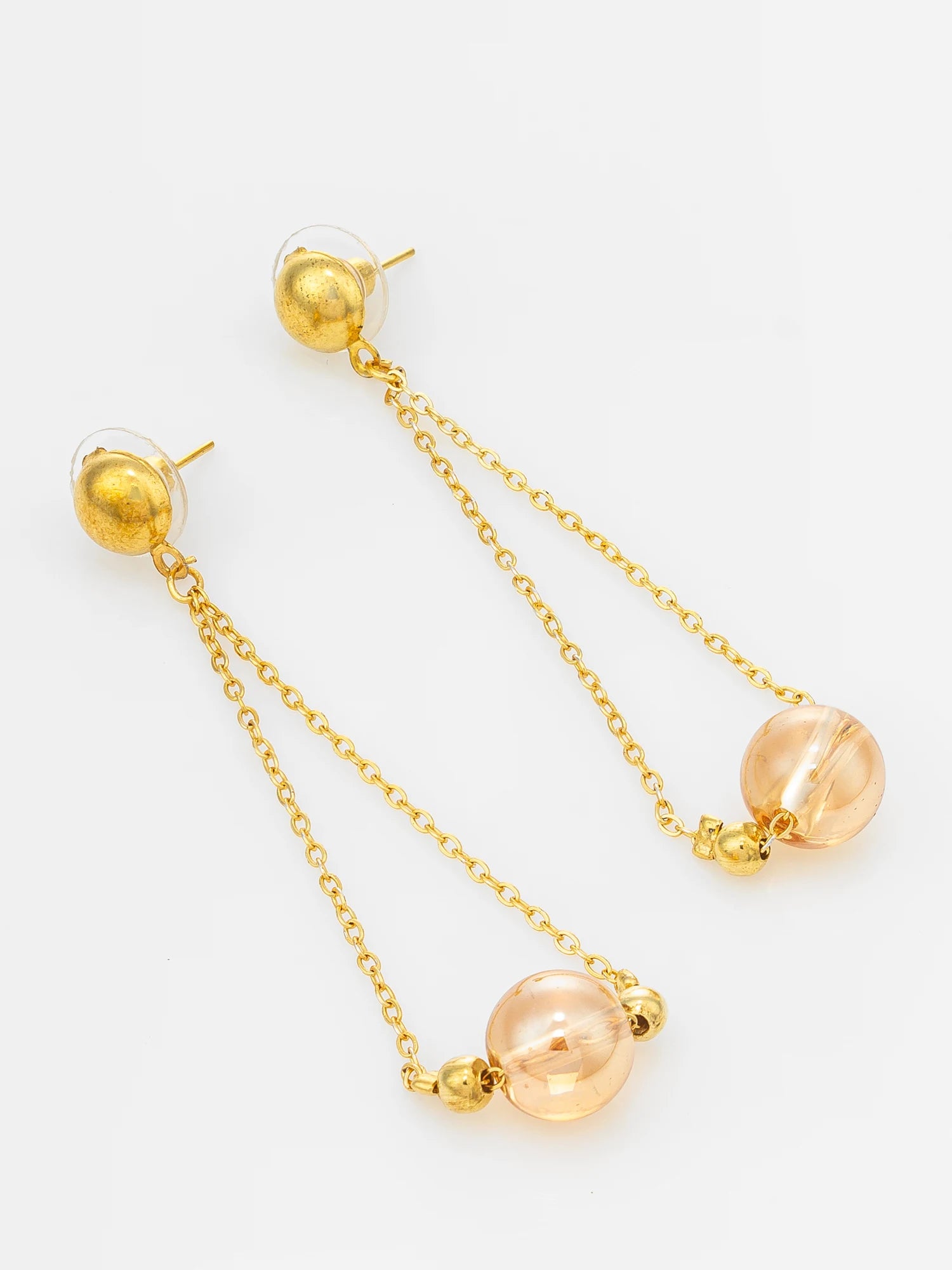 A pair of gold dangle earrings with a textured gold ball stud, a thin gold chain, and a large peach-colored glass bead at the end, displayed on a clean white background.