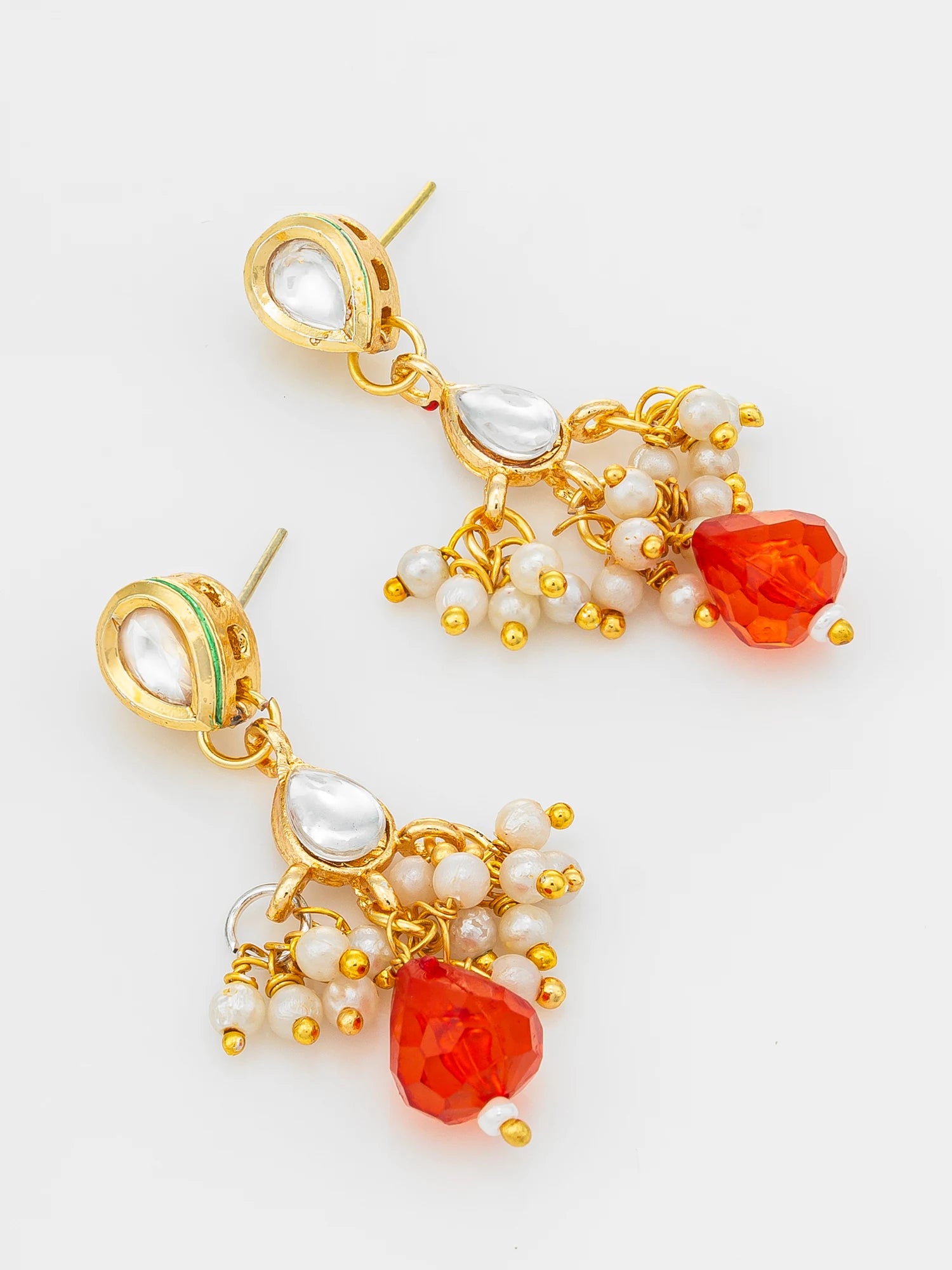 A pair of gold-plated dangle earrings featuring white faux pearls, a small green enamel accent, and faceted orange-red gemstone drops, shown on a clean white background.