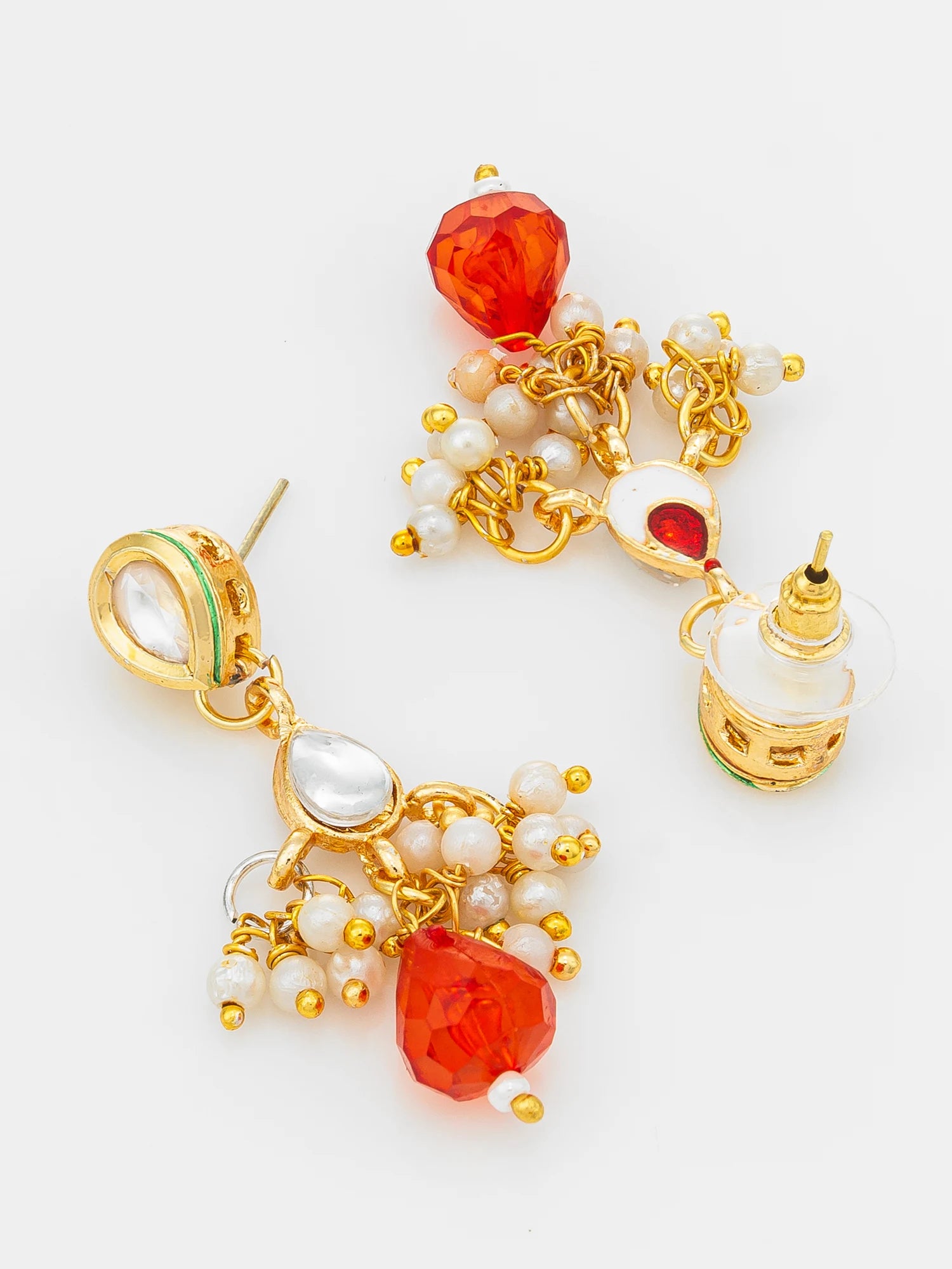 A pair of gold-toned traditional Indian-style dangle earrings featuring faceted orange-red beads, white pearl-like beads, and a small white temple-shaped charm, displayed on a clean white background.