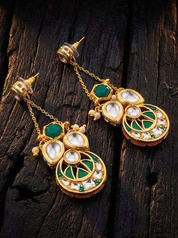 A pair of gold-toned Kalka earrings with green and white stone inlay, displayed on a dark textured wooden surface.