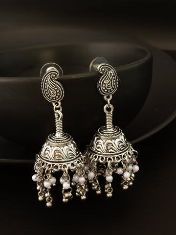 A pair of ornate silver-toned jhumka earrings with paisley-shaped studs, intricate filigree detailing, and dangling pearl-like beads, displayed against a dark background.