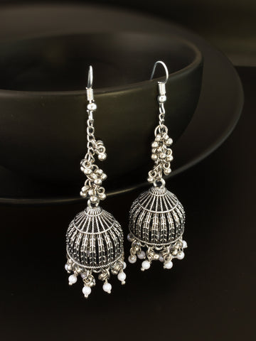 A pair of silver-toned filigree dangle earrings with small white bead accents, displayed against a dark black background.