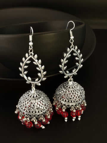 A pair of silver-toned Indian jhumka earrings with red bead accents, displayed against a dark background.