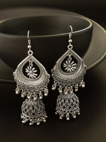 A pair of ornate silver-toned Indian jhumka earrings with intricate filigree work and dangling bell-shaped charms, displayed against a dark background.