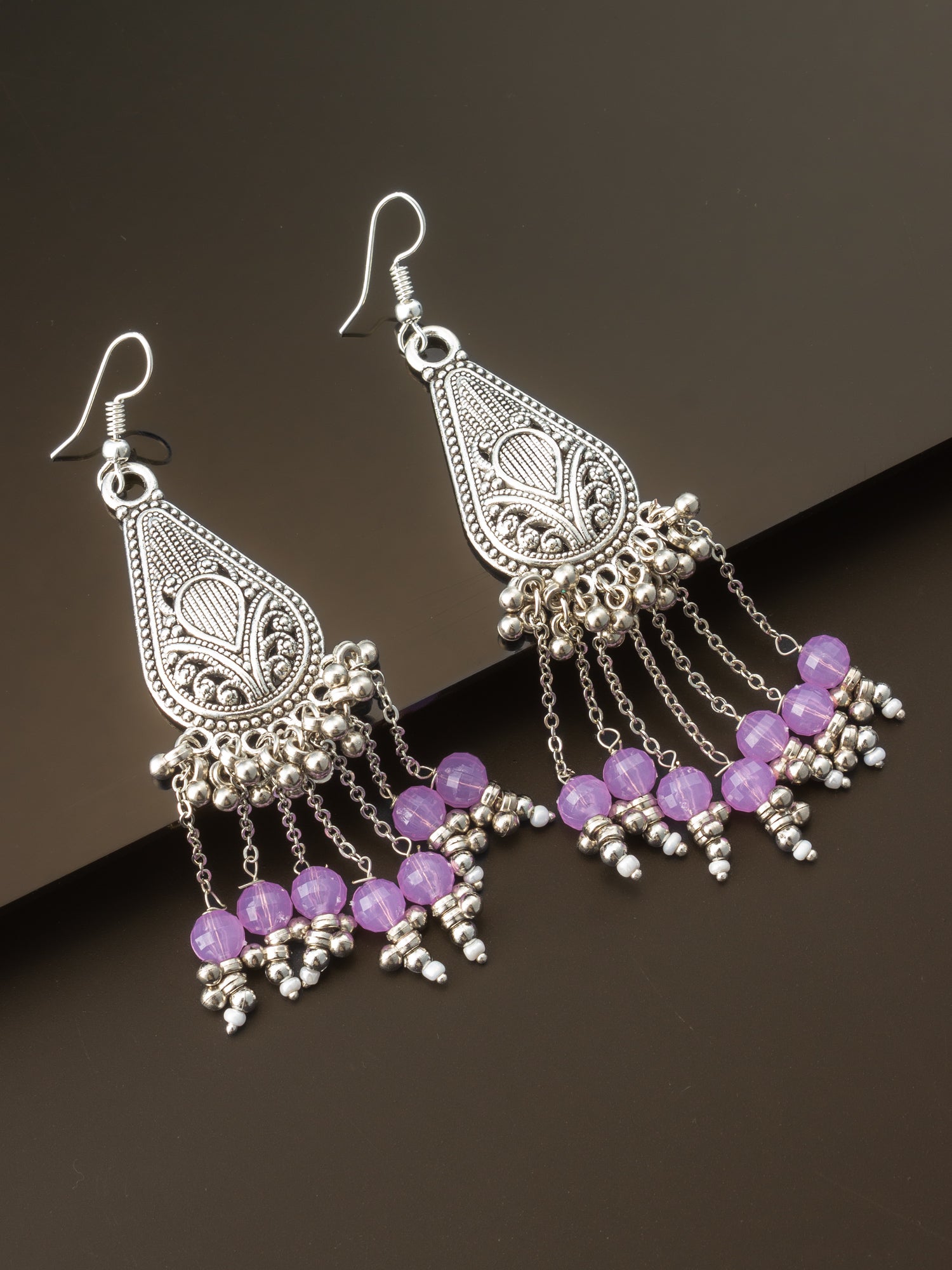 A pair of silver-toned filigree dangle earrings with purple faceted beads and small silver bead accents, displayed on a dark brown background.