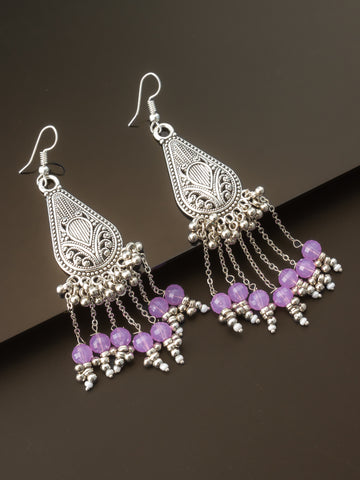 A pair of silver-toned filigree dangle earrings with purple faceted beads and small silver bead accents, displayed on a dark brown background.