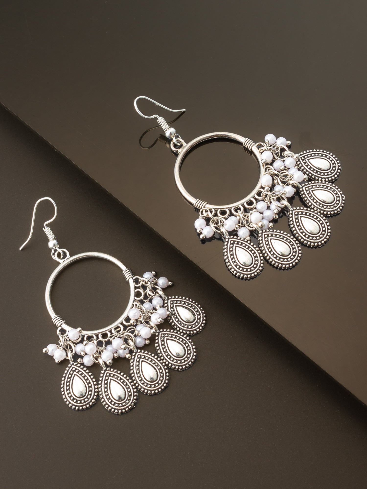 A pair of silver-toned bohemian dangle earrings with white pearl-like beads, displayed on a dark brown background.