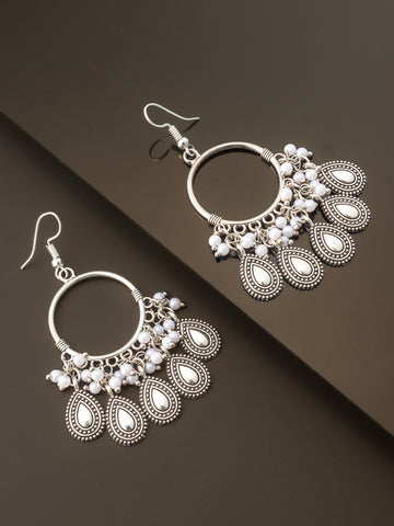 A pair of silver-toned bohemian dangle earrings with white pearl-like beads, displayed on a dark brown background.