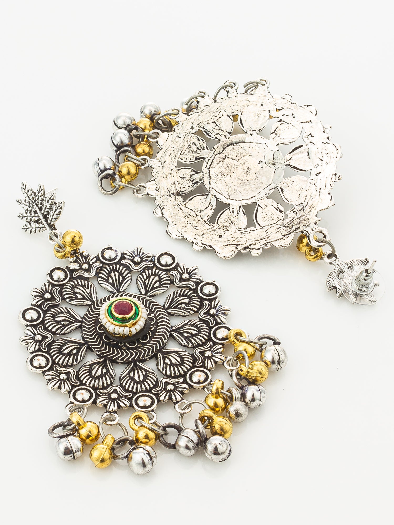 Two ornate silver-toned jewelry pieces with floral filigree, dangling bells, and small gold bead accents on a plain light background. One piece has a central red and green stone, and both have textured silver metalwork.