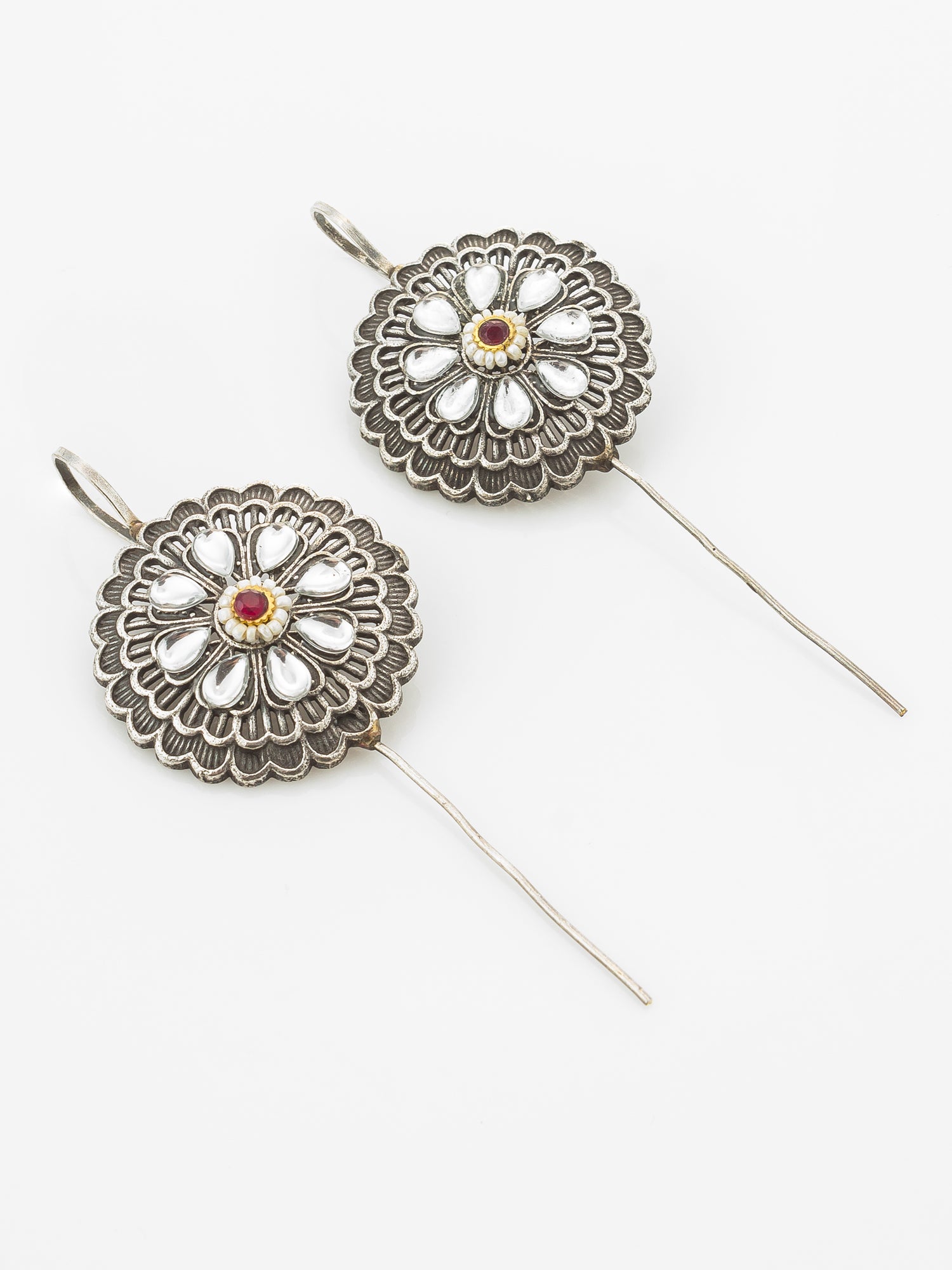 A pair of silver-toned dangle earrings with circular floral filigree pendants featuring white inlay petals and a small red center stone, shown on a plain white background.