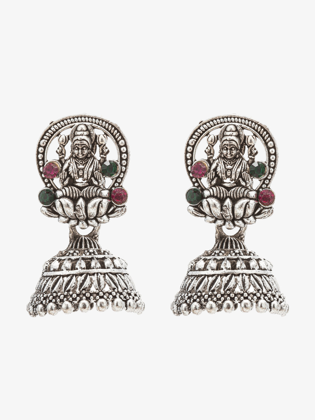 A pair of silver-toned Indian jhumka earrings featuring detailed deity designs and small green and red gemstone accents, displayed on a dark reflective surface.
