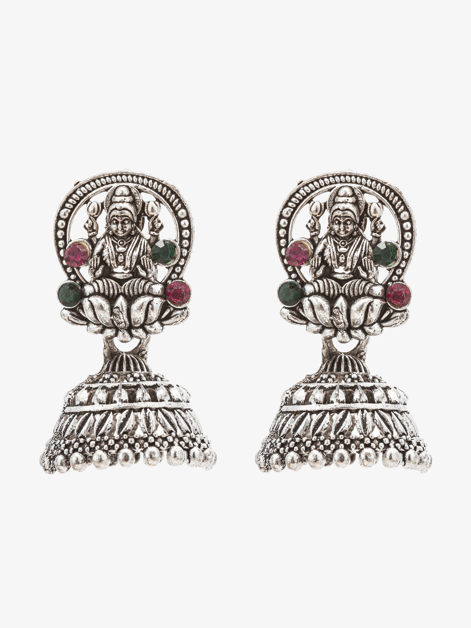 A pair of silver-toned Indian jhumka earrings featuring an embossed deity motif and small green and red gemstone accents, set against a plain white background.