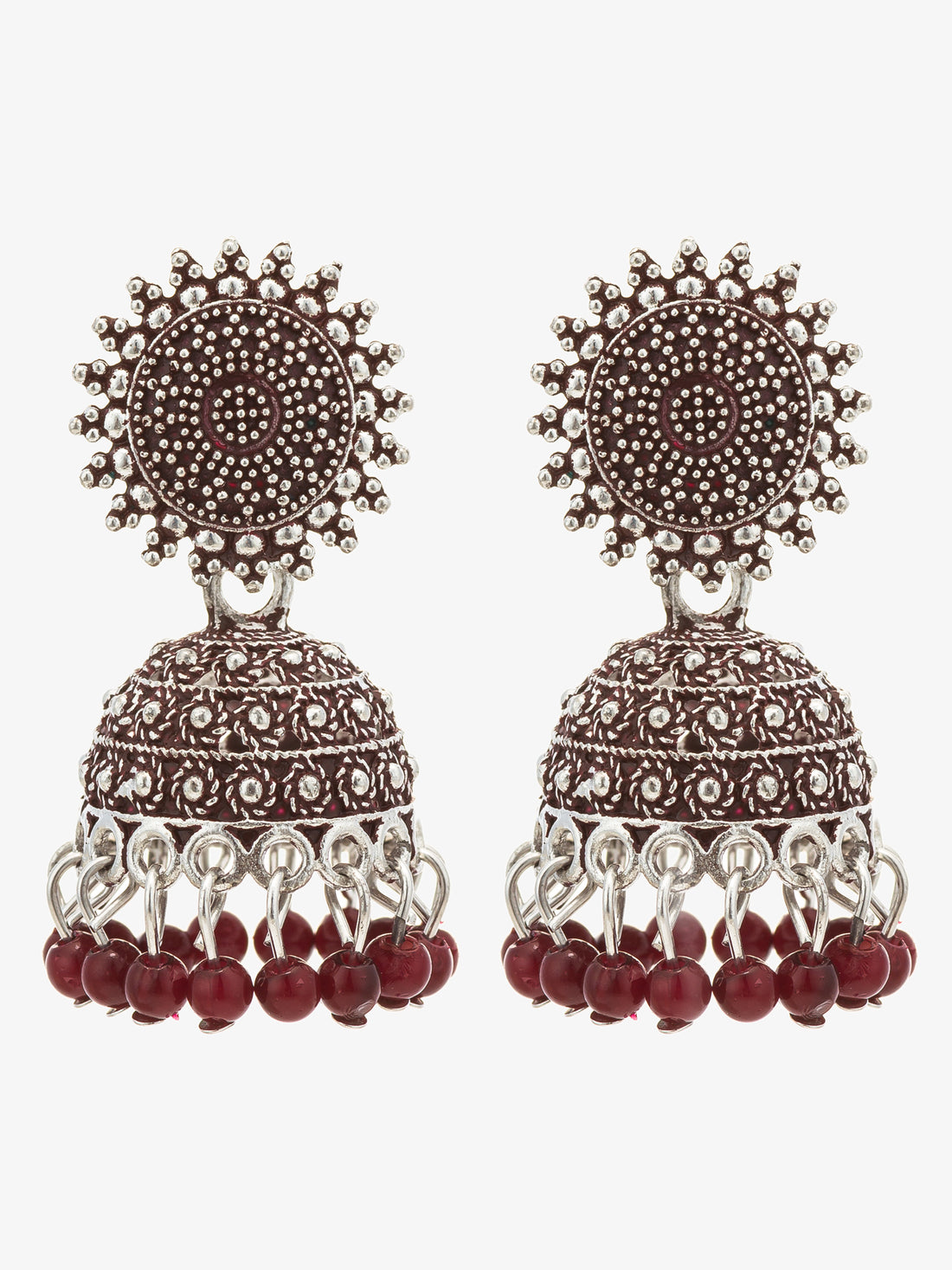 A pair of traditional Indian jhumka earrings with silver-toned metalwork, red stones, and dangling red bead tassels, displayed on a dark glossy surface.