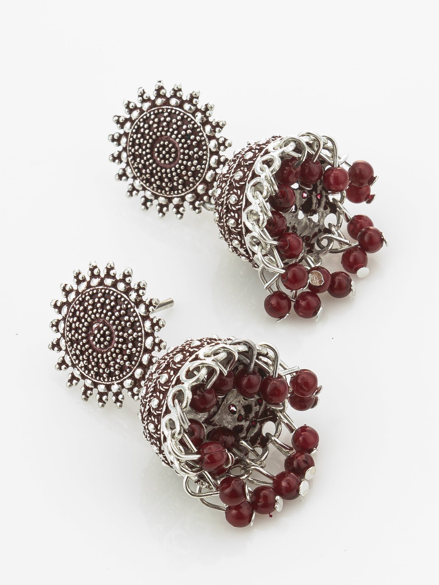 A pair of silver-toned jhumka earrings with dark red bead accents, displayed on a clean white background.
