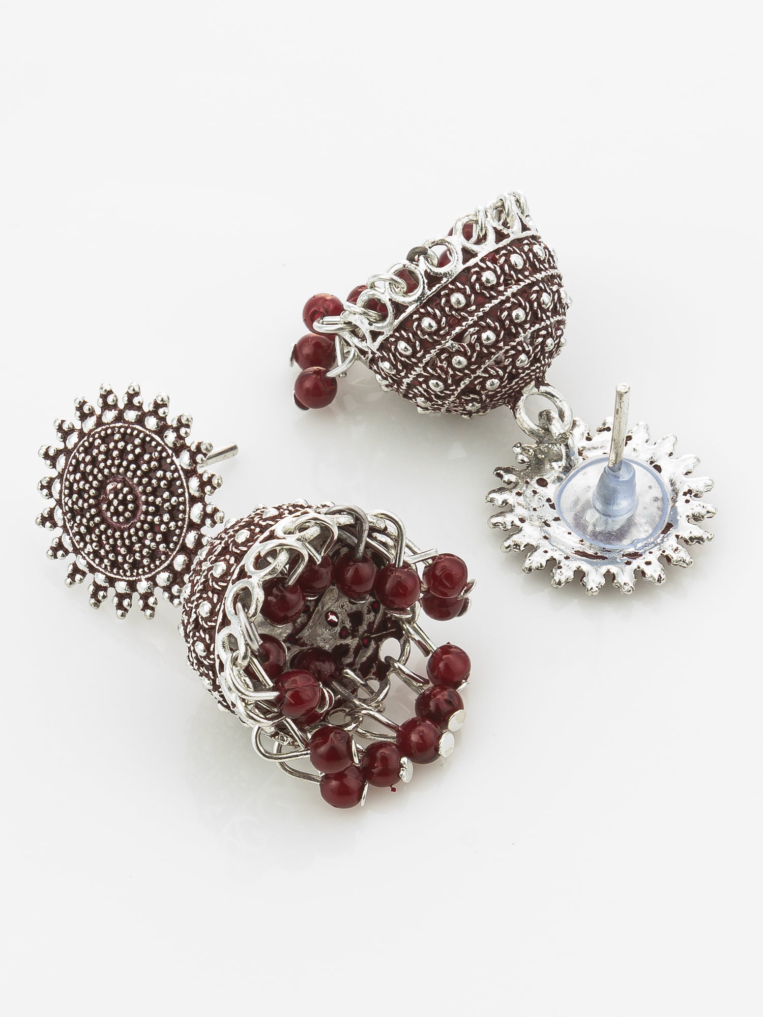 A pair of traditional Indian jhumka earrings with silver-toned filigree, deep red bead drops, and one earring featuring a light blue stone, displayed on a clean white background.