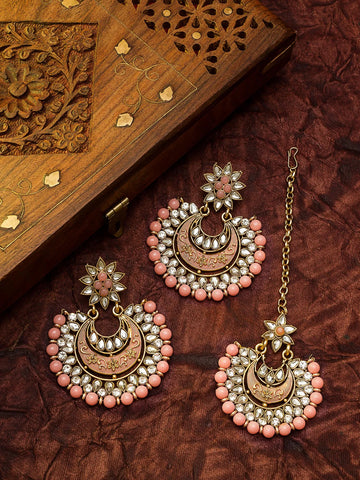 Gold-toned traditional Indian jhumka earrings with pink stone accents and white stones, displayed alongside a matching chain and a carved wooden box on a textured dark brown fabric background.