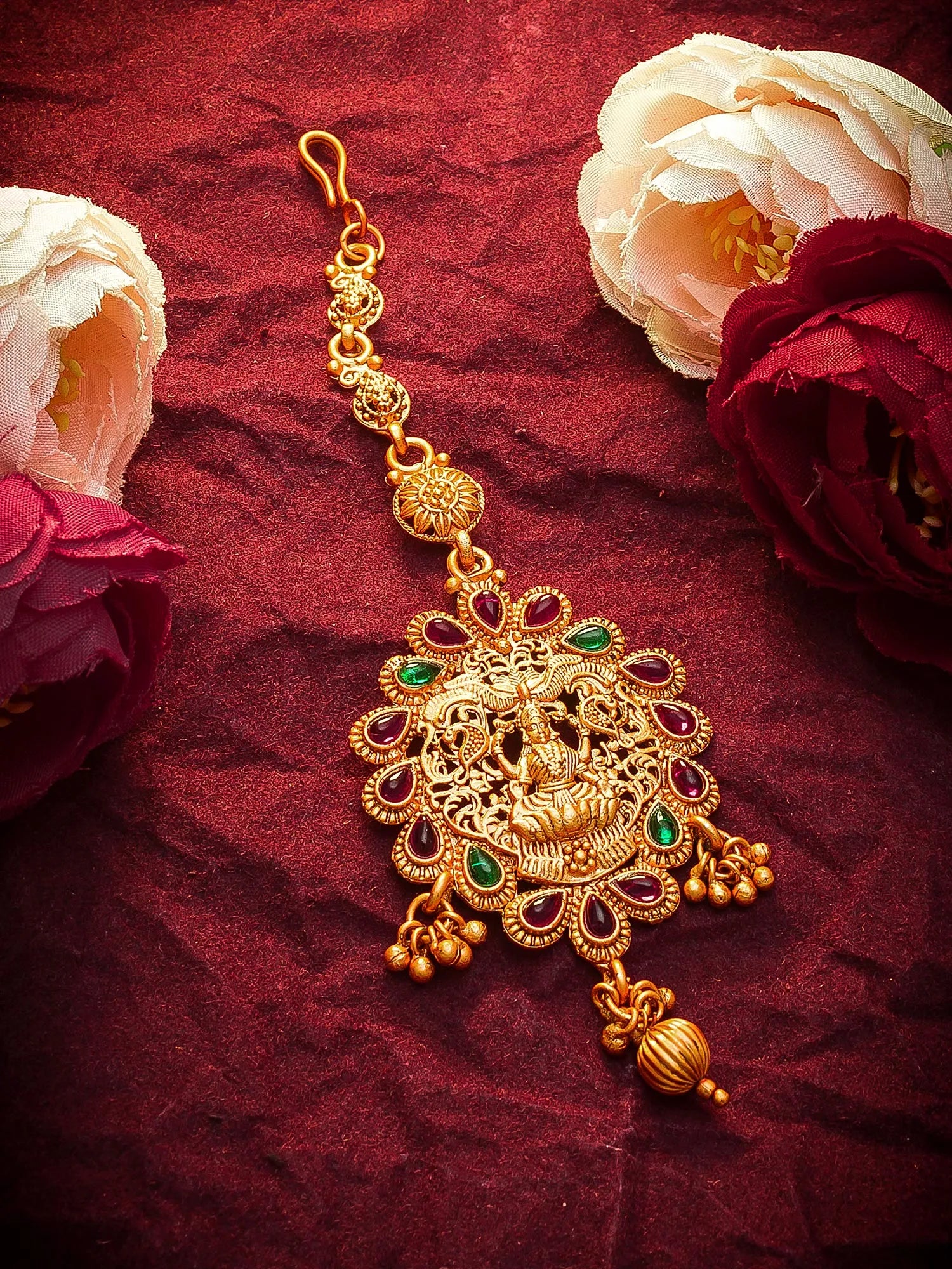 Gold decorative item with green stones on a red fabric background with flowers.
