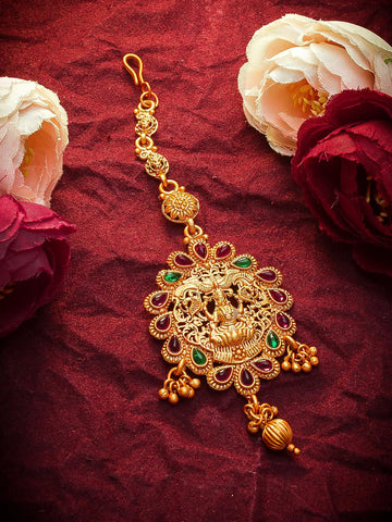 Gold decorative item with green stones on a red fabric background with flowers.