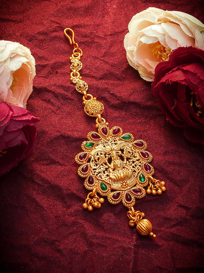 Gold decorative item with green stones on a red fabric background with flowers.