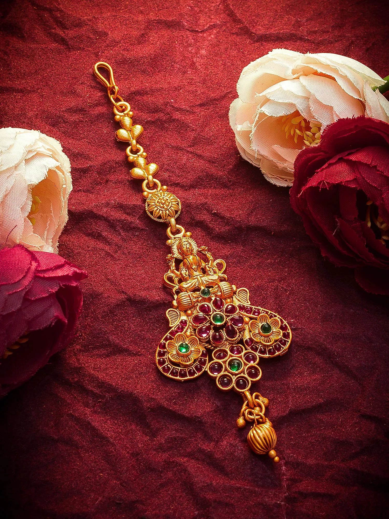 Gold decorative item with green gemstones on a red fabric background with flowers.