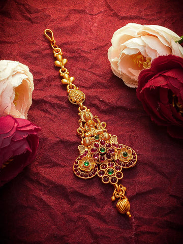 Gold decorative item with green gemstones on a red fabric background with flowers.