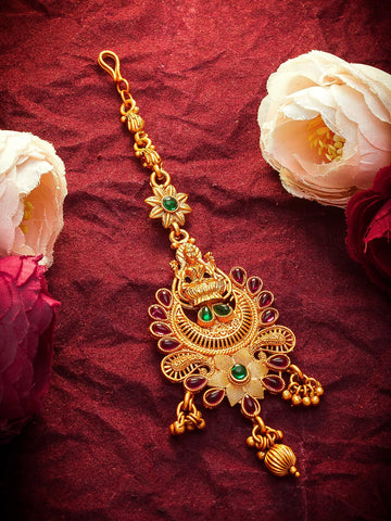 Gold decorative pendant with green gemstones on a red fabric background with flowers.