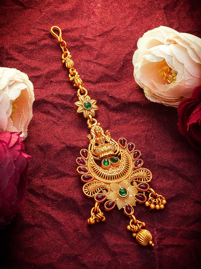 Gold decorative pendant with green gemstones on a red fabric background with flowers.