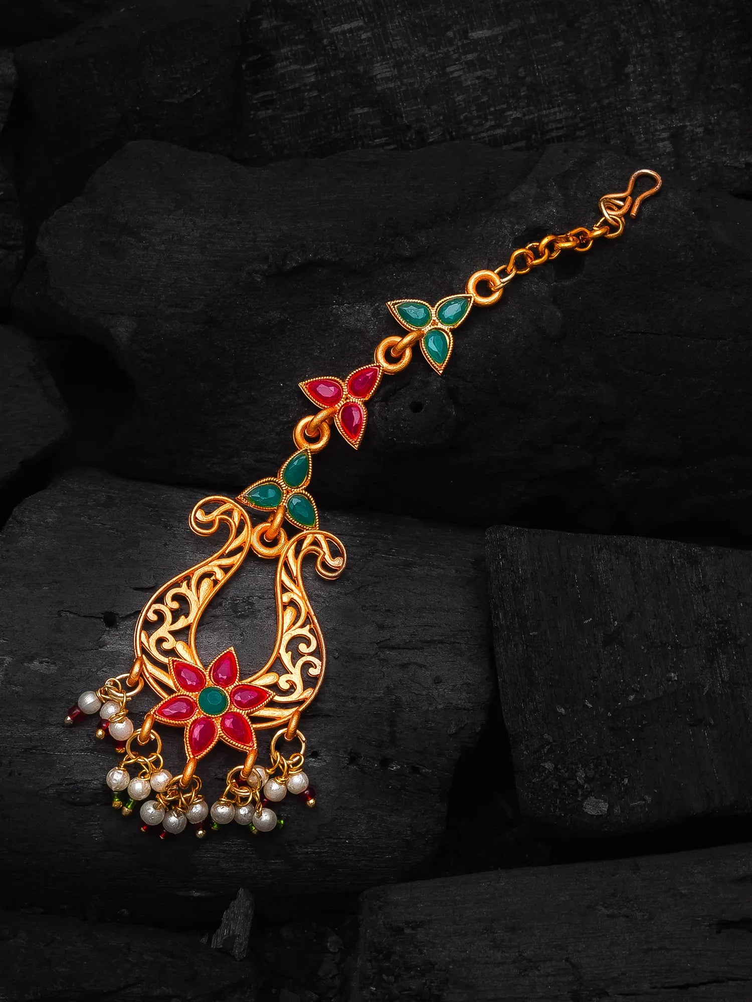 Decorative gold necklace with red and green gemstones on a dark stone background