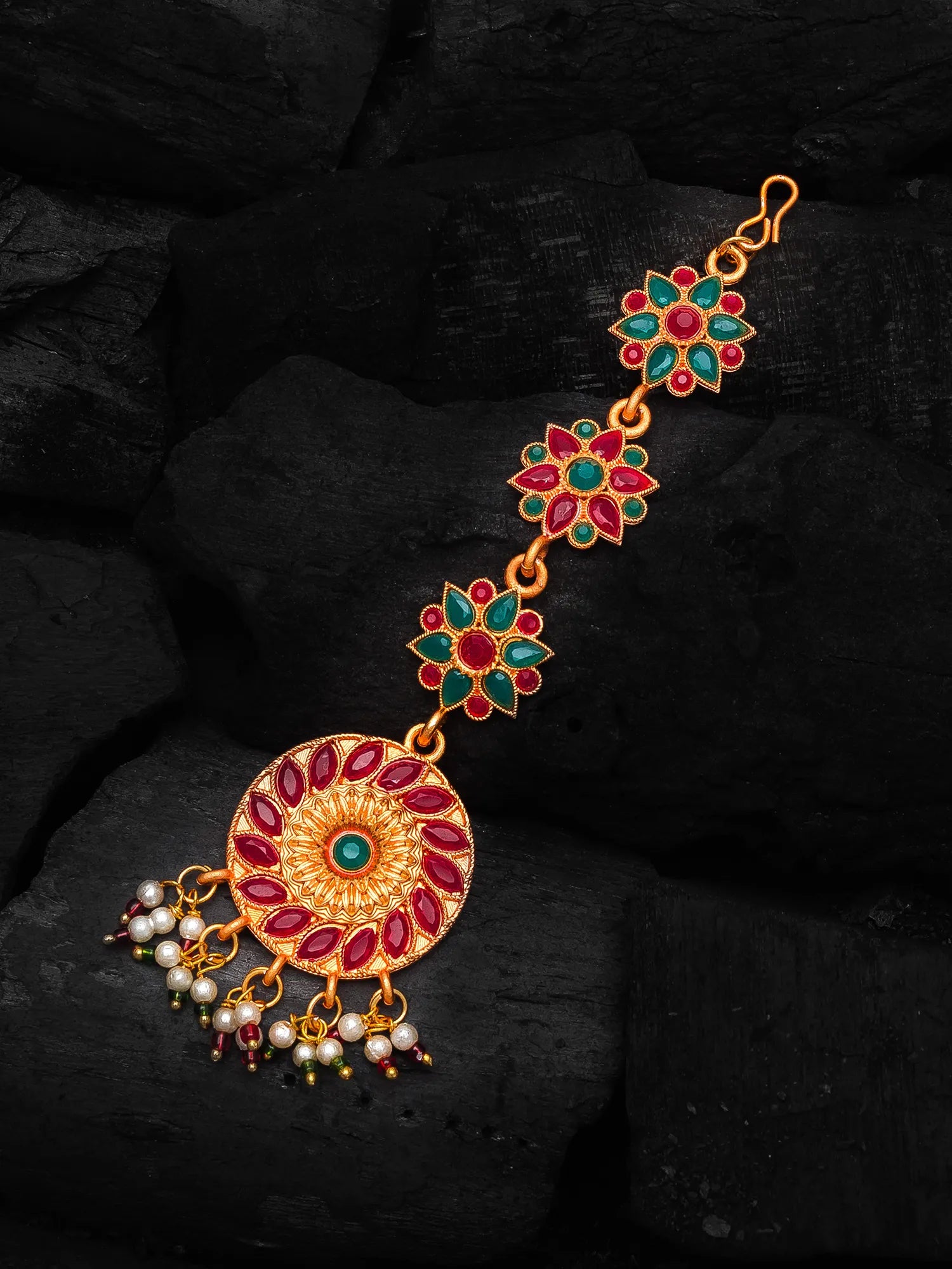 Decorative gold bracelet with red and green gemstones on a dark background