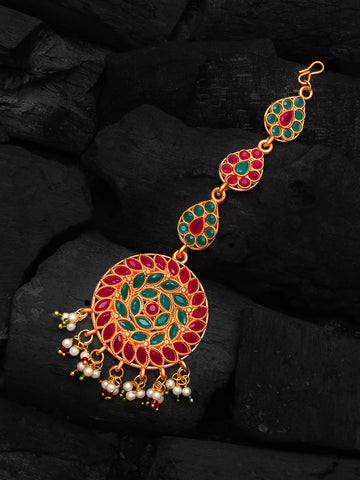 Decorative gold bracelet with red and green stones on a dark stone background