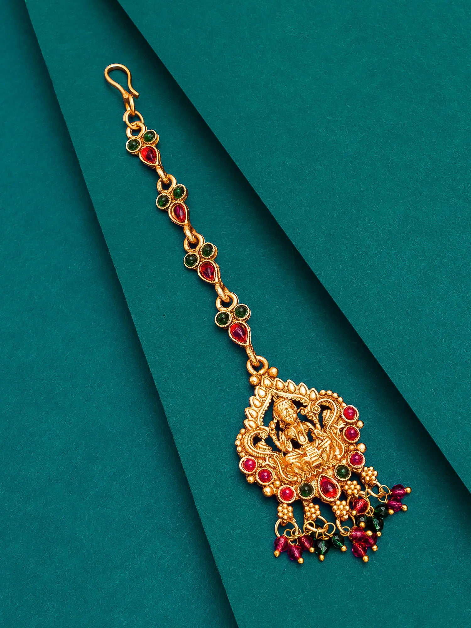 Gold and red gemstone decorative hair accessory on a teal background