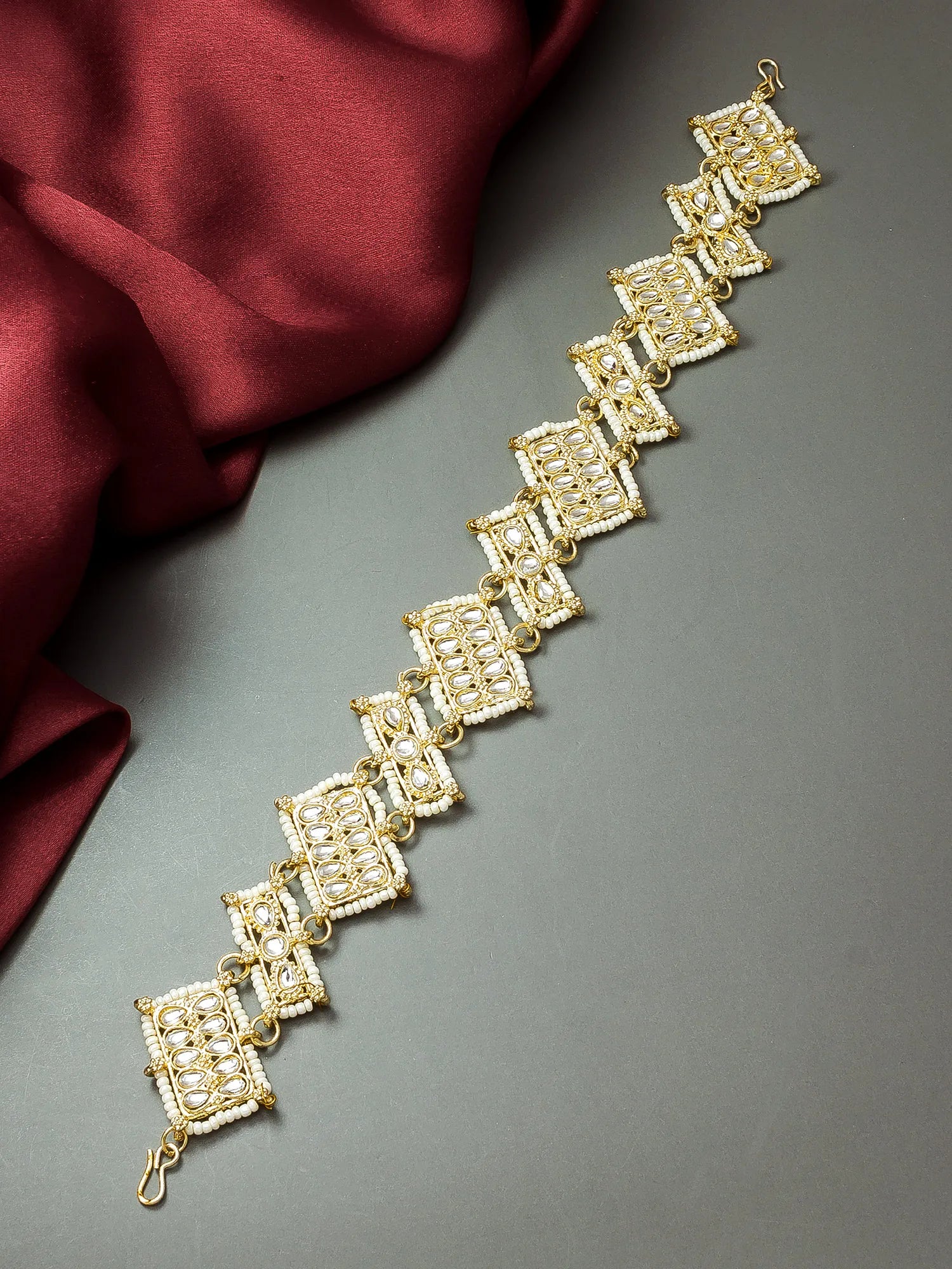 Gold bracelet on a gray surface with a red fabric background