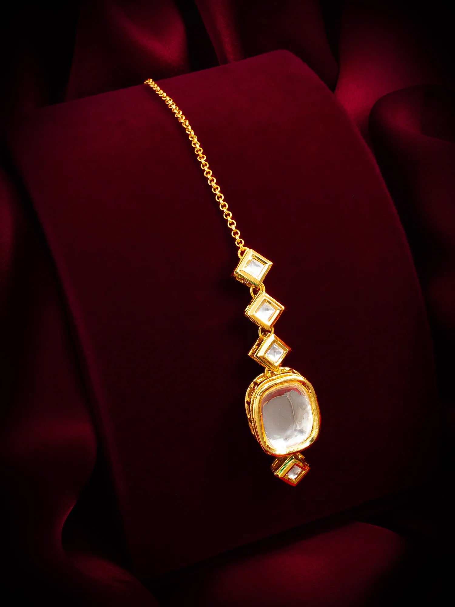 Gold necklace with a pendant on a dark red fabric background