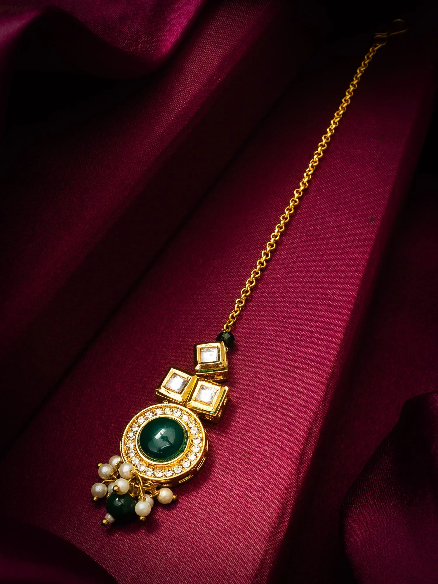 Gold necklace with green gemstone and pearl pendants on a maroon fabric background