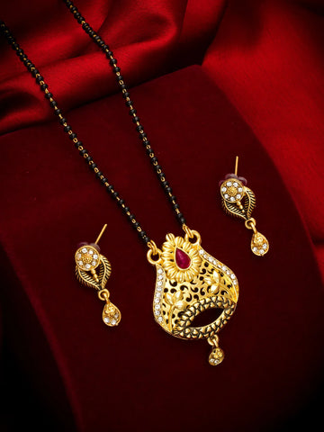 Gold-toned traditional Indian jewelry set featuring a necklace with a detailed filigree pendant, matching drop earrings, and a black beaded chain, displayed on a rich red satin background.